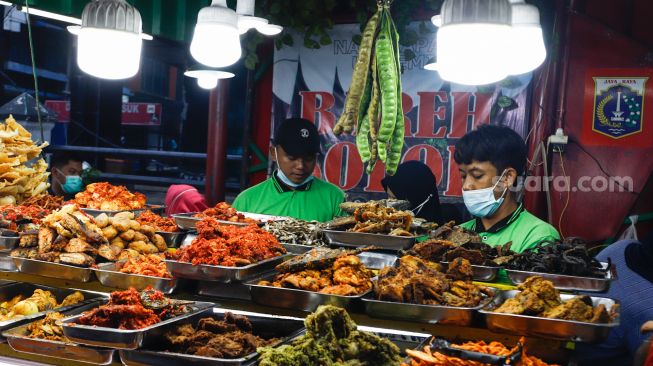 Pelayan mengambil menu makanan di Sentra kuliner Nasi Kapau di Jalan Kramat Raya, Senen, Jakarta Pusat, Selasa (12/4/2021). [Suara.com/Alfian Winanto]