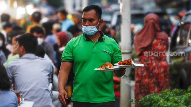 Pelayan mengantar makanan di Sentra kuliner Nasi Kapau di Jalan Kramat Raya, Senen, Jakarta Pusat, Selasa (12/4/2021). [Suara.com/Alfian Winanto]