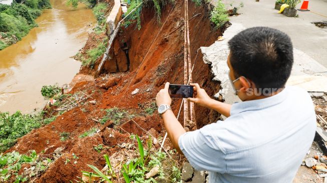 Warga melihat lokasi longsor didaerah bantaran sungai Ciliwung, Pengadegan Timur, Pancoran, Jakarta Selatan, Selasa (12/4/2022). [Suara.com/Alfian Winanto]