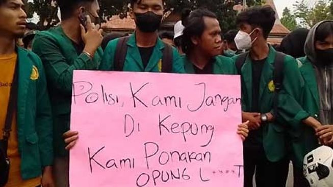 Mahasiswa yang tergabung dalam Aliansi Mahasiswa Riau membentangkan poster lucu bernada satire di depan Gedung DPRD Riau, Senin (11/4/2022). [Suara.com/Wahid Irawan]