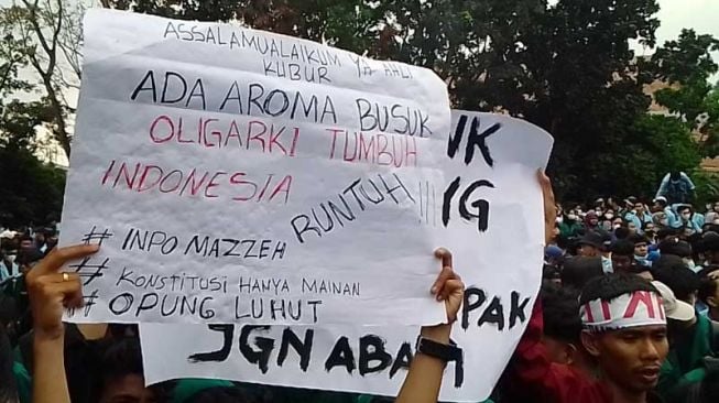 Mahasiswa yang tergabung dalam Aliansi Mahasiswa Riau membentangkan poster lucu bernada satire di depan Gedung DPRD Riau, Senin (11/4/2022). [Suara.com/Wahid Irawan]