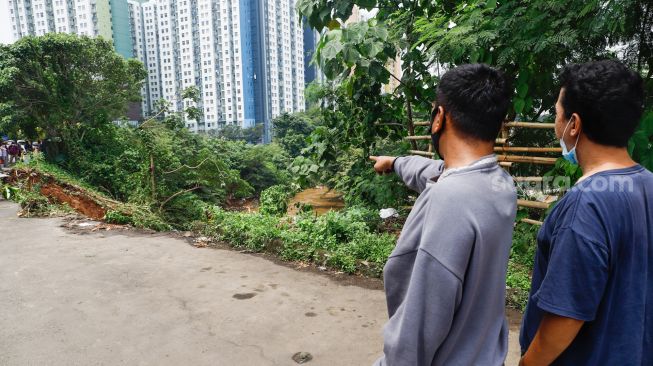 Warga melihat lokasi longsor didaerah bantaran sungai Ciliwung, Pengadegan Timur, Pancoran, Jakarta Selatan, Selasa (12/4/2022). [Suara.com/Alfian Winanto]