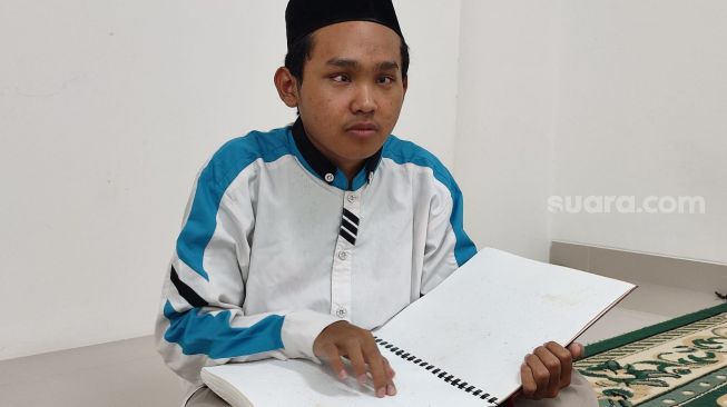 Zaenal Abidin, santri tunanetra di Pesantren Raudlatul Makfufin, Kota Tangerang Selatan (Tangsel), tengah membaca Al Quran dengan mushaf braile. [Suara.com/Wivy Hikmatullah]