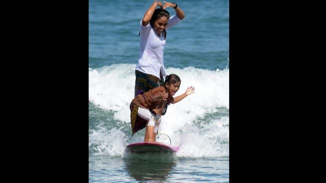 Peselancar wanita bersama anaknya mengenakan kebaya saat beratraksi di Pantai Kuta, Badung, Bali, Sabtu (16/4/2022). [ANTARA FOTO/Nyoman Hendra Wibowo/rwa]