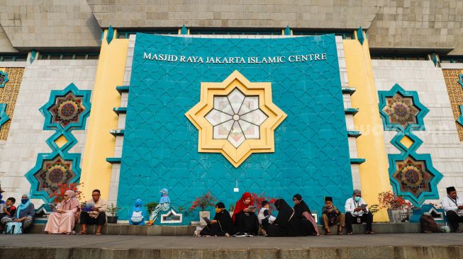 Umat Islam membaca Al-Quran sambil menunggu waktu berbuka puasa di halaman Masjid Raya Jakarta Islamic Center, Jakarta Utara, Senin (18/4/2022). [Suara.com/Alfian Winanto]