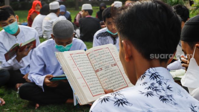 Umat Islam membaca Al-Quran sambil menunggu waktu berbuka puasa di halaman Masjid Raya Jakarta Islamic Center, Jakarta Utara, Senin (18/4/2022). [Suara.com/Alfian Winanto]