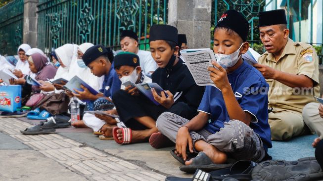 Umat Islam membaca Al-Quran sambil menunggu waktu berbuka puasa di halaman Masjid Raya Jakarta Islamic Center, Jakarta Utara, Senin (18/4/2022). [Suara.com/Alfian Winanto]