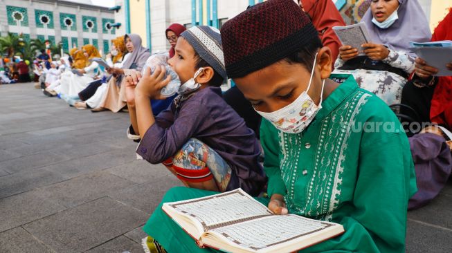 Umat Islam membaca Al-Quran sambil menunggu waktu berbuka puasa di halaman Masjid Raya Jakarta Islamic Center, Jakarta Utara, Senin (18/4/2022). [Suara.com/Alfian Winanto]