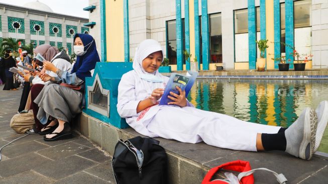 Umat Islam membaca Al-Quran sambil menunggu waktu berbuka puasa di halaman Masjid Raya Jakarta Islamic Center, Jakarta Utara, Senin (18/4/2022). [Suara.com/Alfian Winanto]