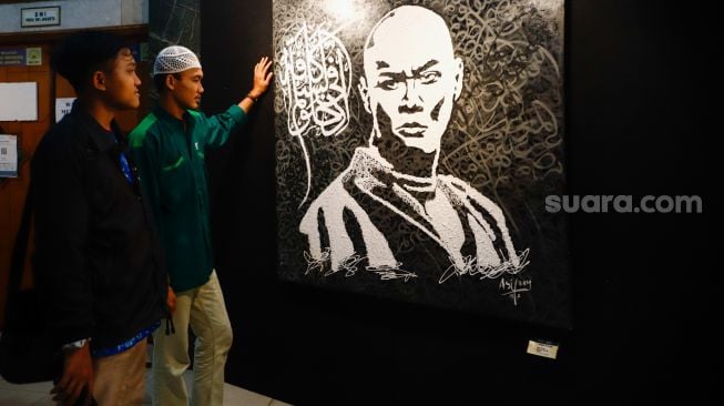 Pengunjung melihat kaligrafi bergambar tokoh Presenter dan Pesulal Deddy Corbuzier dalam Pameran Kaligrafi Kontemporer Internasional di Masjid Raya Jakarta Islamic Center, Jakarta Utara, Senin (18/4/2022). [Suara.com/Alfian Winanto]