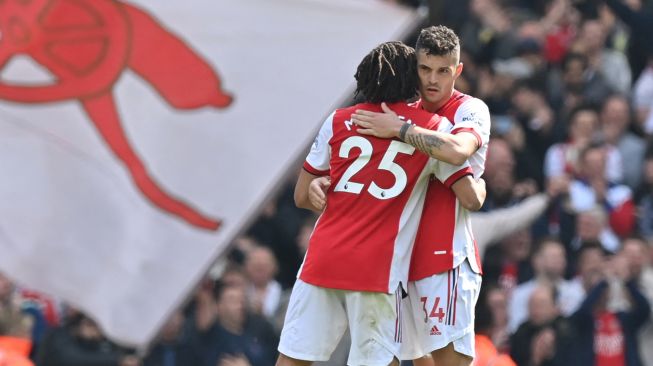 Gelandang Arsenal Granit Xhaka (kanan) memeluk gelandang Arsenal Mohamed Elneny saat mereka berselebrasi di lapangan usai pertandingan sepak bola Liga Premier Inggris antara Arsenal dan Manchester United di Stadion Emirates, London, Inggris, Sabtu (23/4/2022). [Glyn KIRK / AFP]