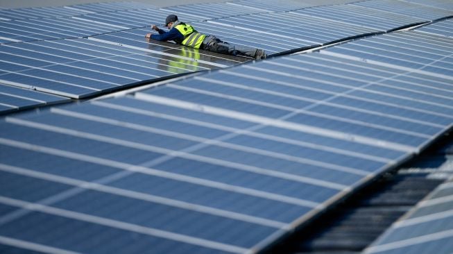 Seorang pekerja merakit panel surya di pembangkit fotovoltaik terapung di danau Silbersee, Haltern, Jerman, Jumat (22/4/2022). [Ina FASSBENDER / AFP]
