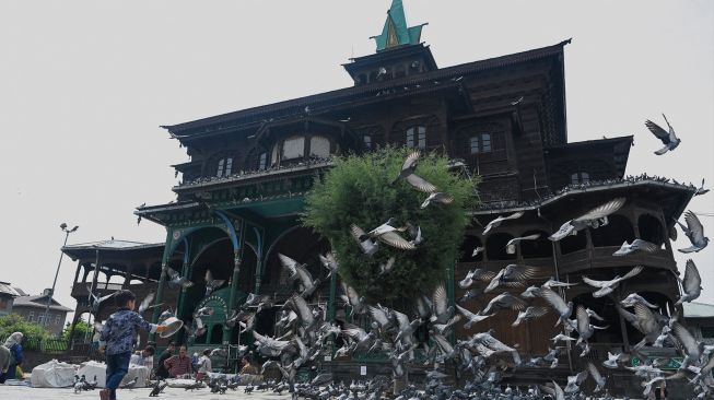 Seorang anak laki-laki memberi makan merpati saat bulan suci Ramadhan di Masjid Khanqah Shah, Srinagar, India, Rabu (13/4/2022). [TAUSEEF MUSTAFA / AFP]