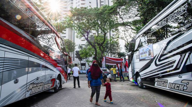 Pemudik berjalan di dekat bus dalam Mudik Gratis Polri 2022 di kompleks Gelora Bung Karno, Jakarta, Senin (25/4/2022). [ANTARA FOTO/Sigid Kurniawan/aww]