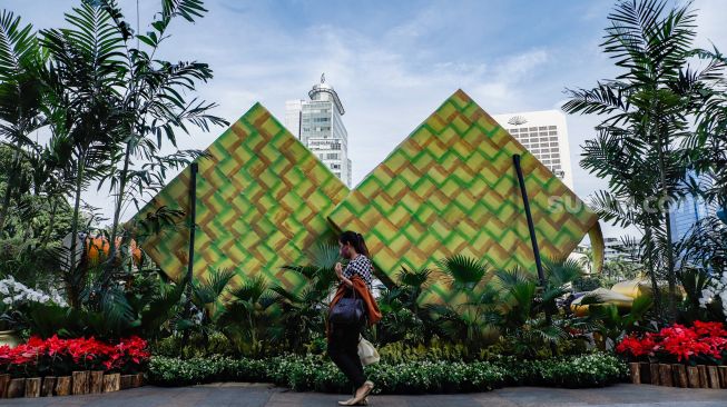 Warga melintasi ornamen bernuansa lebaran yang terpasang di kawasan Bundaran HI, Jakarta Pusat, Selasa (26/4/2022). [Suara.com/Alfian Winanto]