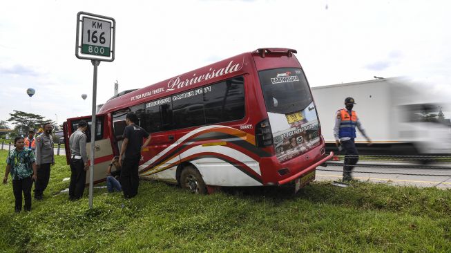 Sejumlah personel polisi melihat kondisi sebuah mini bus yang bernopol E 7506 KC usai mengalami kecelakaan tunggal di kilometer 166 Tol Palimanan-CIkampek, Jawa Barat, Selasa (26/4/2022).  ANTARA FOTO/M Risyal Hidayat
