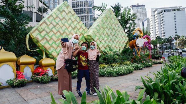 Warga berswafoto dengan latar belakang ornamen bernuansa lebaran yang terpasang di kawasan Bundaran HI, Jakarta Pusat, Selasa (26/4/2022). [Suara.com/Alfian Winanto]