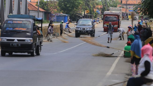 Sejumlah warga menunggu pengendara motor memberi sedekah dengan melempar uang di Jembatan Sewo, Jalur Pantura Sukra Indramayu, Jawa Barat, Senin (25/4/2022).  ANTARA FOTO/Dedhez Anggara
