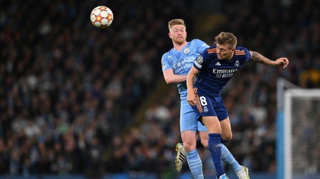 Gelandang Manchester City dari Belgia, Kevin De Bruyne (kiri) berebut bola dengan gelandang Real Madrid asal Jerman Toni Kroos selama pertandingan leg pertama semifinal Liga Champions antara Manchester City vs Real Madrid, di Stadion Etihad, di Manchester, pada April 26, 2022.Paul ELLIS / AFP.