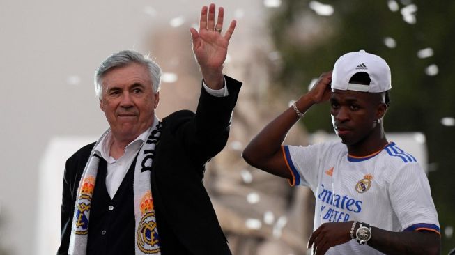 Pelatih Real Madrid asal Italia Carlo Ancelotti (kiri) dan pemain depan Real Madrid asal Brasil Vinicius Junior menyapa para fans di alun-alun Plaza Cibeles di Madrid dalam perade juara Liga Spanyol 2021/2022. Real Madrid menjadi kampiun Liga Spanyol 2022 setelah mengalahkan Espanyol 4-0 dalam laga pekan ke-34 pada 30 April 2022. OSCAR DEL POZO / AFP.