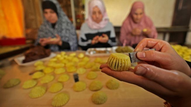 Wanita Palestina membuat kue tradisional Maamoul yang berisi kurma dan kacang-kacangan untuk persiapan hari raya Idul Fitri di kota Hebron, Palestina, Kamis (28/4/2022). [HAZEM BADER / AFP]