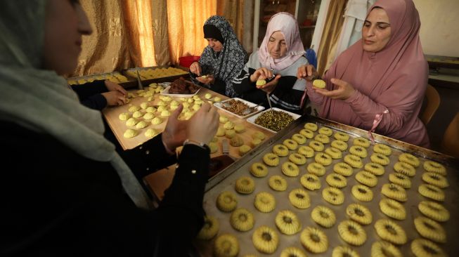 Wanita Palestina membuat kue tradisional Maamoul yang berisi kurma dan kacang-kacangan untuk persiapan hari raya Idul Fitri di kota Hebron, Palestina, Kamis (28/4/2022). [HAZEM BADER / AFP]