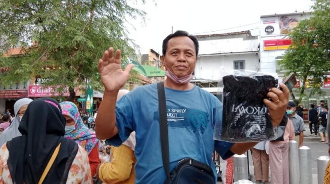  I Nengah Sutaga,  warga Kalimantan yang berlibur ke Jogja menerima kaos dari Presiden Jokowi saat berbelanja di Teras Malioboro 2, Kota Jogja, Minggu (1/5/2022). [Muhammad Ilham Baktora/ SuaraJogja.id]