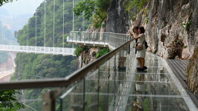 Pengunjung berdiri di pinggir jembatan kaca Bach Long di distrik Moc Chau, Son La, Vietnam, Jumat (29/4/2022). [Nhac NGUYEN / AFP]