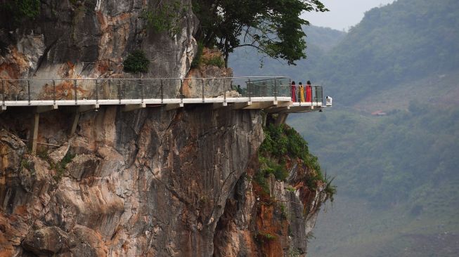 Pengunjung berdiri di pinggir jembatan kaca Bach Long di distrik Moc Chau, Son La, Vietnam, Jumat (29/4/2022). [Nhac NGUYEN / AFP]