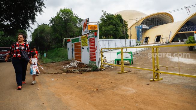 Pengunjung melintas di depan Teater Keong Mas yang sedang direvitalisasi di Taman Mini Indonesia Indah, Jakarta Timur, Rabu (4/5/2022). [Suara.com/Alfian Winanto]