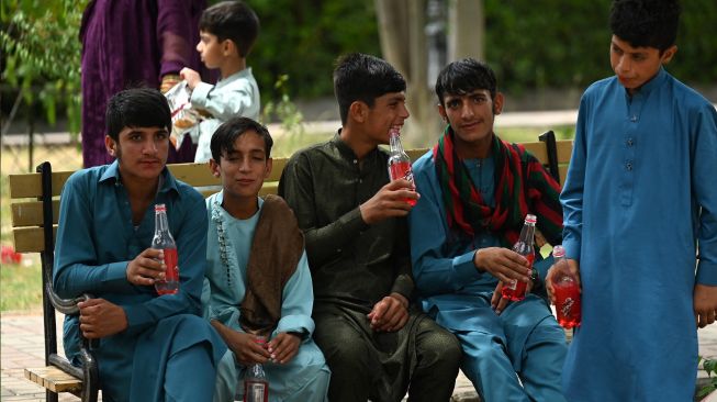 Anak-anak minum sambil duduk di pinggir danau saat hari raya Idul Fitri di Islamabad, Pakistan, Selasa (3/5/2022). [Aamir QURESHI / AFP]