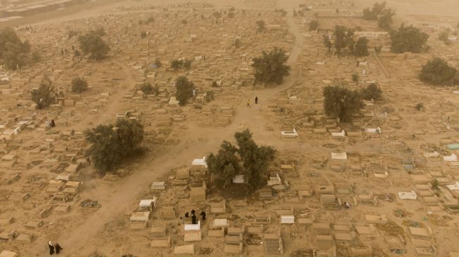 Foto udara menunjukkan warga muslim Irak mengunjungi makam kerabat mereka saat badai pasir pada hari pertama Idul Fitri di pemakaman Hassan al-Basri di Distrik Zubayr, Basra, Irak, Senin (2/5/2022). [Hussein Faleh / AFP]
