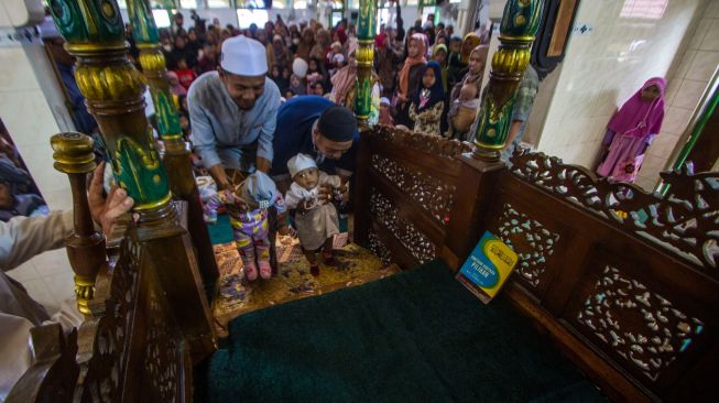 Pengurus masjid menuntun balita menjejakkan kaki untuk naik ke atas mimbar tempat khatib berkhotbah saat tradisi Batumbang Apam di Masjid Al Munawwarah, Barabai, Kabupaten Hulu Sungai Tengah, Kalimantan Selatan, Rabu (4/5/2022). [ANTARA FOTO/Bayu Pratama S/tom]
