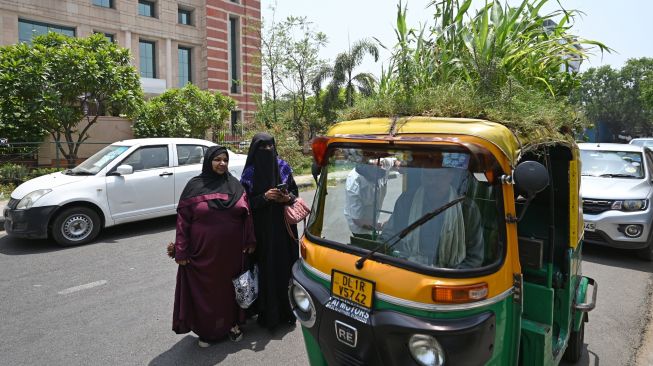Orang-orang berbicara dengan pengemudi Bajaj Mahender Kumar saat dia duduk di kendaraannya di New Delhi, India, Senin (2/5/2022). [Money SHARMA / AFP]