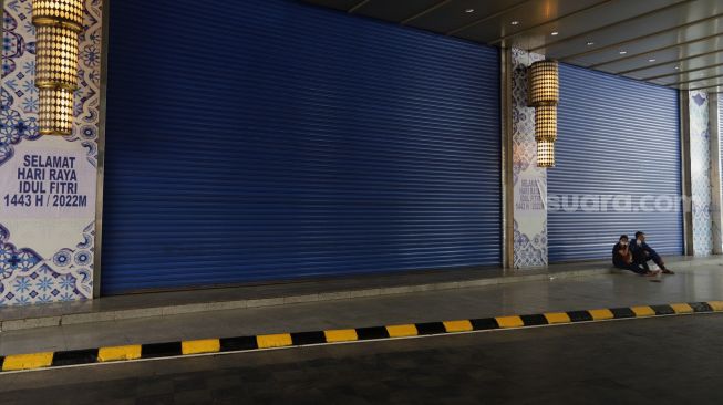 Warga duduk di depan pintu masuk Pasar Tanah Abang Blok A, Jakarta, Kamis (5/5/2022). [Suara.com/Angga Budhiyanto]