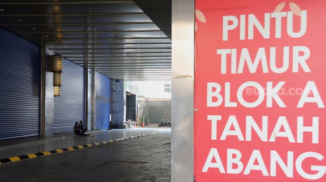 Warga duduk di depan pintu masuk Pasar Tanah Abang Blok A, Jakarta, Kamis (5/5/2022). [Suara.com/Angga Budhiyanto]