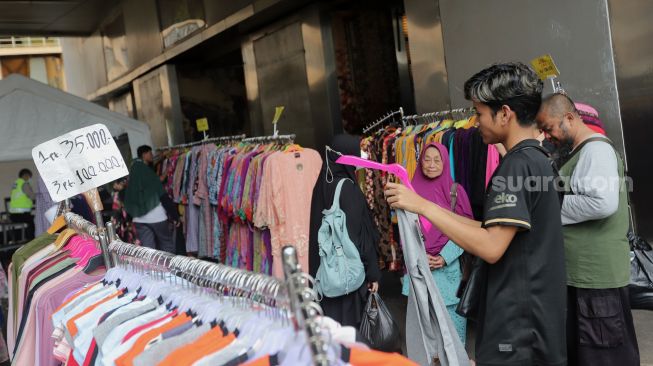 Pedagang pakaian melayani pembeli di depan pintu masuk Pasar Tanah Abang Blok A, Jakarta, Kamis (5/5/2022). [Suara.com/Angga Budhiyanto]
