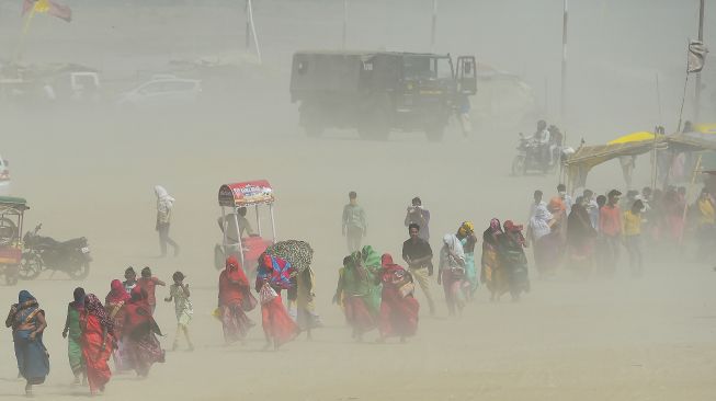 Warga berjalan di tengah badai pasir di Sangam, pertemuan sungai Gangga, Yamuna, dan Saraswati pada sore musim panas di Allahabad, India, pada (23/4/2022). [SANJAY KANOJIA / AFP]