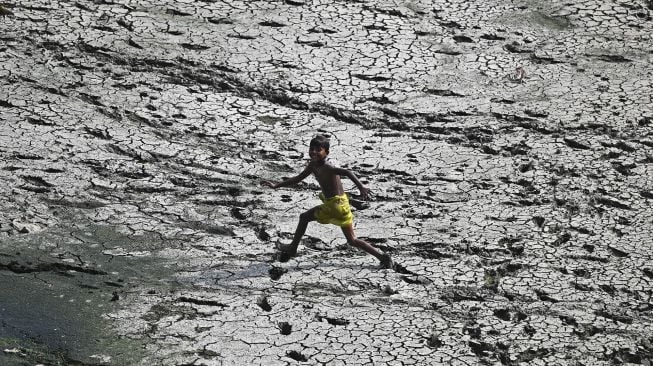 Seorang anak laki-laki berlari melintasi sepetak dasar sungai Yamuna yang kering pada hari musim panas di New Delhi, India, pada (2/5/2022). [Sajjad HUSSAIN / AFP]