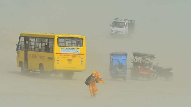 Warga berjalan di tengah badai pasir di Sangam, pertemuan sungai Gangga, Yamuna, dan Saraswati pada sore musim panas di Allahabad, India, pada (23/4/2022). [SANJAY KANOJIA / AFP]