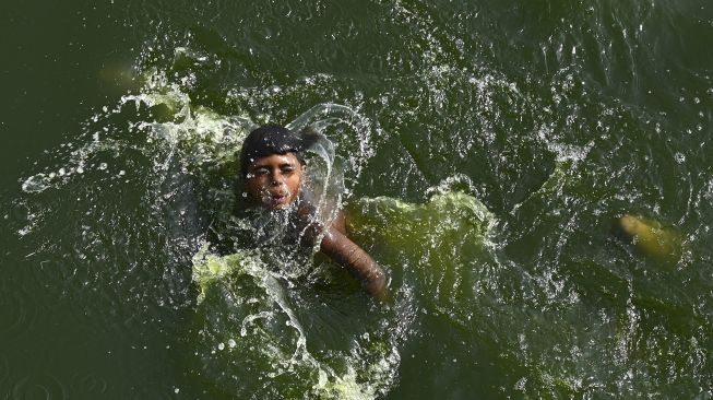 Seorang anak laki-laki mendinginkan dirinya di perairan sungai Yamuna pada hari musim panas di New Delhi, India, pada (2/5/2022). [Sajjad HUSSAIN / AFP]