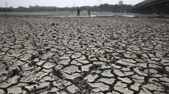 Warga berjalan melintasi sepetak dasar sungai Yamuna yang kering pada hari musim panas di New Delhi, India, pada (2/5/2022). [Sajjad HUSSAIN / AFP]