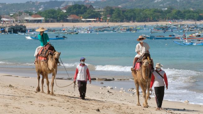 Wisatawan menikmati suasana pantai dengan menaiki unta saat liburan di Pantai Kelan, Badung, Bali, Sabtu (7/5/2022). [ANTARA FOTO/Nyoman Hendra Wibowo/tom]