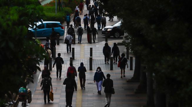 Sejumlah pekerja berjalan di trotoar saat jam pulang kerja di Jalan Sudirman, Jakarta Pusat, Senin (9/5/2022). [Suara.com/Alfian Winanto]