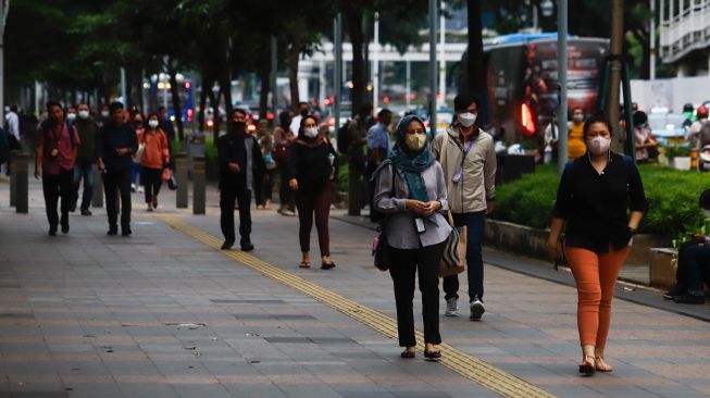 Sejumlah pekerja berjalan di trotoar saat jam pulang kerja di Jalan Sudirman, Jakarta Pusat, Senin (9/5/2022). [Suara.com/Alfian Winanto]