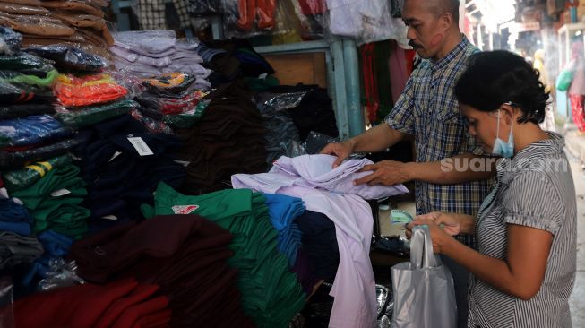 Pedagang seragam sekolah melayani calon pembeli di Pasar Jatinegara, Jakarta, Rabu (11/5/2022). [Suara.com/Angga Budhiyanto]