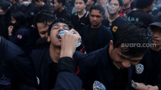 Massa mahasiswa Universitas Trisakti memberikan minuman kepada temannya saat menggelar aksi unjuk rasa memperingati Tragedi Trisakti 1998 di kawasan Patung Kuda Arjuna Wiwaha, Jakarta, Kamis (12/5/2022). [Suara.com/Angga Budhiyanto] 