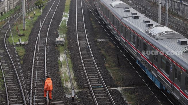 Seorang petugas berjalan di samping rangkaian KRL Commuter Line yang melintas di kawasan Tanah Abang, Jakarta, Jumat (13/5/2022). [Suara.com/Angga Budhiyanto]