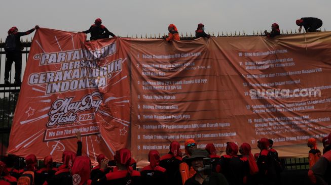 Massa buruh memasang spanduk saat melakukan aksi unjuk rasa di depan gedung DPR RI, Jakarta, Sabtu (14/5/2022). [Suara.com/Angga Budhiyanto]