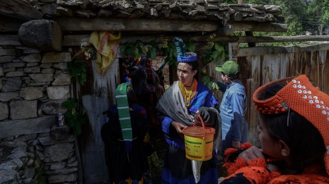 Wanita suku Kalash yang mengenakan pakaian tradisional berjalan menuju rumah kerabat mereka untuk mengumpulkan susu dan menari sebagai bagian dari ritual pada hari pertama festival 'Joshi' di desa Bumburet, Pakistan, Sabtu (14/5/2022). [Abdul MAJEED / AFP]
